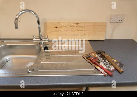 Küchenspüle Installation unvollständig Hand geschrieben Baumeister Zeichen Wasser noch nicht angeschlossen Werkzeuge an der Seite der Entleerungsbrett Edelstahl-Mischbatterie Stockfoto