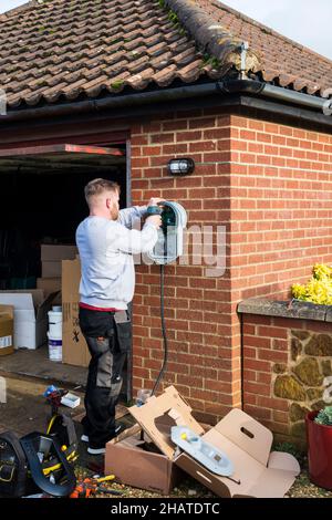 Elektriker, der ein Ladegerät für Elektroautos von Zappi an die Außenwand einer privaten Garage montiert. NB: Die Räumlichkeiten auf dem Foto sind Eigentum freigegeben. Stockfoto