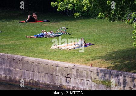 Blick auf Menschen, die sich im heißen Sommer auf grünem Gras zum Entspannen und Sonnenbaden an der Spree niederlassen. Stockfoto