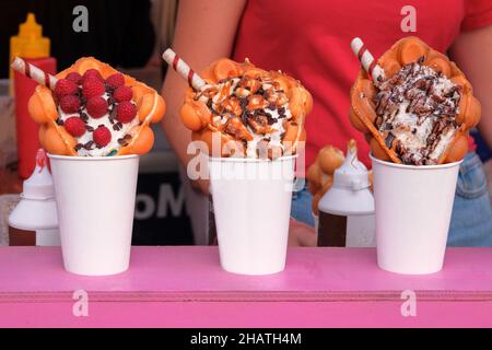 Blasenwaffeln mit Himbeeren, Schokolade, Marschmalow und Nüssen in weißen Pappbechern werden auf dem Food Festival-Event verkauft. Street Sweet Dessert in Food sta Stockfoto