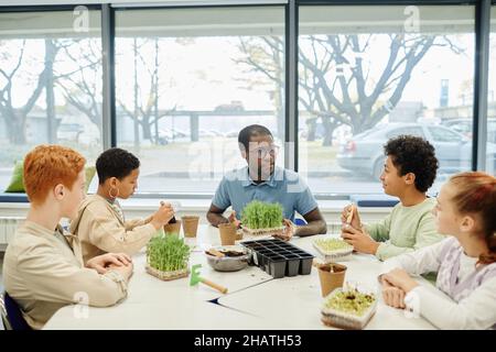 Verschiedene Gruppe von Kindern, die Samen Pflanzen, während sie in der Biologie-Klasse in der Schule mit afroamerikanischem Lehrer experimentierten Stockfoto