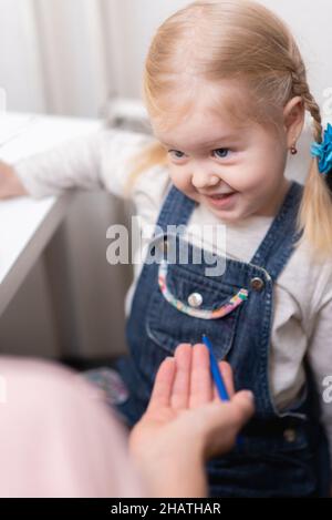 Die Sprechtherapeutin hilft dem kleinen Mädchen, ihre Rede in ihrem Büro zu korrigieren Stockfoto