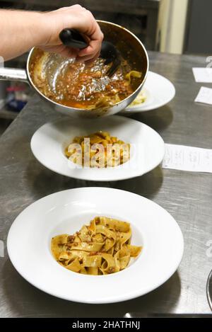 Von oben der Ernte anonymen Koch Putting appetitlich freche Tagliatelle Pasta aus der Pfanne in Keramikplatten auf dem Tisch in der Restaurantküche platziert Stockfoto