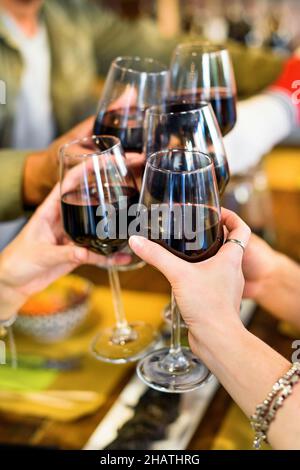 Schneiden Sie eine anonyme Gruppe von Freunden, die in einem hellen, modernen Restaurant mit Rotwein klirren, während Sie gemeinsam eine festliche Veranstaltung am Tisch feiern Stockfoto