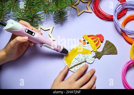 Ein Mädchen zeichnet einen Schneemann mit einem 3d-Stift auf einem violetten Hintergrund Stockfoto