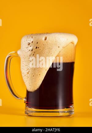 Dunkelbraunes Bier in einem halben Liter Glas-Becher, isoliert auf gelbem Hintergrund Stockfoto