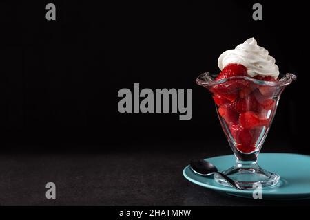 Erdbeeren und Schlagsahne in Eiscreme auf schwarzem Hintergrund Stockfoto