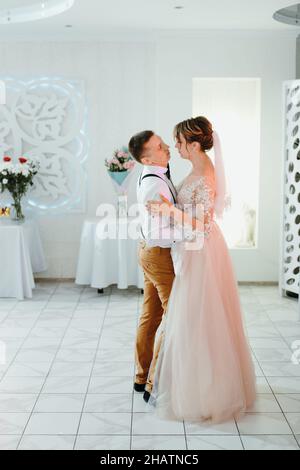 Das wunderschöne kaukasische Paar heiratete gerade und tanzte ihren ersten Tanz. Gerade verheiratetes Paar, das vor ihren unkenntlichen Freunden tanzt. Stockfoto