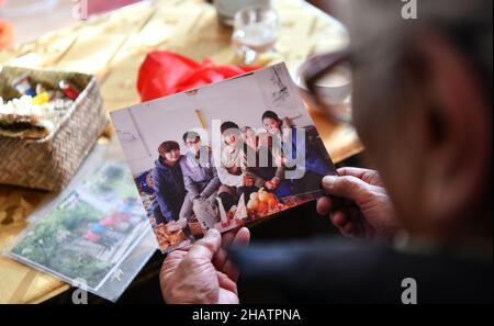 (211215) -- LHASA, 15. Dezember 2021 (Xinhua) -- Tsering Drolma sieht sich ein Gruppenfoto ihrer Enkel mit ihr in ihrem Haus in Lhasa, südwestlich der Autonomen Region Tibet, an, 7. Dezember 2021. Tsering Drolma, geboren 1940, ist Rentner und lebt im Stadtgebiet von Lhasa. Sie war einst Leibeigene und führte in ihrer Kindheit ein elendes Leben. Im Alter von 8 Jahren war sie zu jung, um schwere Arbeit zu verrichten, so dass sie vom Leibeigenen nur wenige Rationen verdienen konnte. Abgesehen von dem Hungertod musste sie die Kälte ertragen, als ihr Leibeigenbesitzer nachts draußen mit Vieh schlief. „Was für ein Glück war es, in den Sonnen zu baden Stockfoto