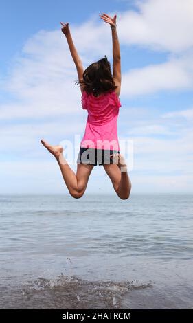 Junges Mädchen mit langen braunen Haaren, die in die Luft bläst, ein Symbol für Glück und Freude im Sommer Stockfoto