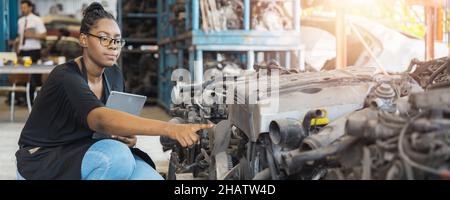 Porträt einer selbstbewussten afrikanischen Frau, die in alten Teilen der Autofabrik nachschaut und arbeitet Stockfoto