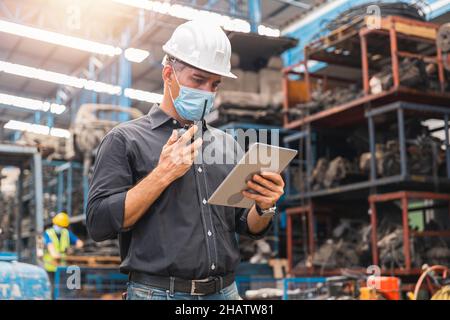 Inspektor Vorarbeiter mit Gesichtsmaske oder Ingenieur Manager Blick auf Tablet und Kontrolle der Arbeit per Funk in der Fabrik Stockfoto