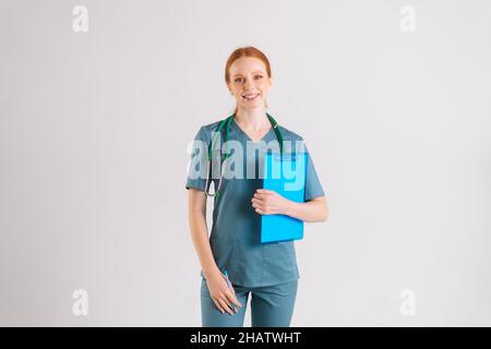 Porträt von fröhlichen hübschen jungen Frau Arzt in medizinischer Uniform hält Zwischenablage und Blick auf die Kamera. Stockfoto