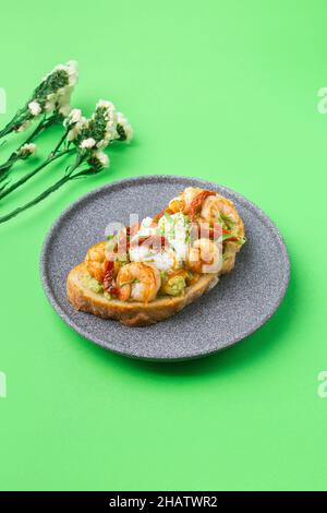 Toast mit Garnelen, Garnelen, Avocado und pochiertem Ei auf grünem Hintergrund mit Blumen Stockfoto