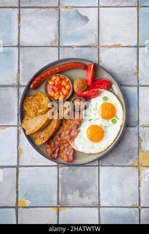 Englisches Frühstück mit Spiegeleiern, Würstchen, Speck, Bohnen, Toast, Tomaten und Pilze Fliesen Hintergrund. Stockfoto