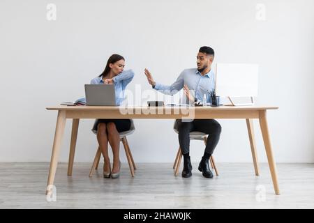 Weibliche Angestellte hustet in Ellenbogen in der Nähe von verängstigten Kollegen Stockfoto