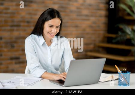 Portrait kaukasische junge Geschäftsfrau im Büro. Attraktive selbstbewusste intelligente Frau Top-Manager oder Händler, Brunette, nutzt Laptop für SMS mit Kollegen oder Kunden, bereitet Geschäftsprojekt Stockfoto