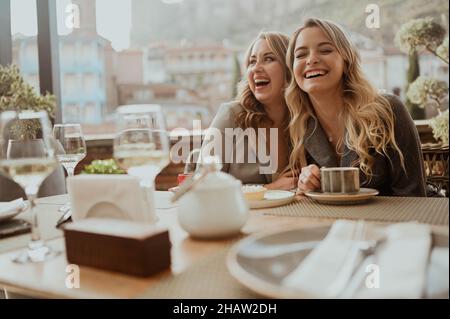 Nahaufnahme Porträt von zwei Freundinnen in strengen Anzügen lachen trinken Kaffee und Wein auf der Terrasse draußen im Sommer Straßencafe auf Hintergrundgebäuden Alte Tiflis Stadt, Georgien. Hochwertige Fotos Stockfoto
