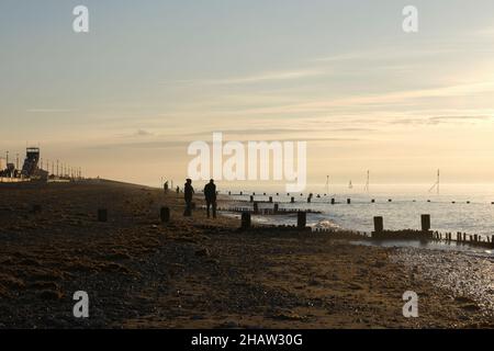 Die Menschen genießen den Sonnenuntergang im Winter beim Wandern und Schwimmen am Strand von Hunstanton im November 2021 Stockfoto