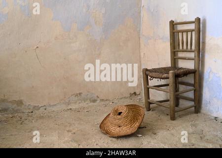 Traditioneller spanischer Stuhl mit Strohhut im alten Haus, Strohhut auf dem Boden vor dem Korbstuhl, Lost Place, Andalusien, Spanien Stockfoto