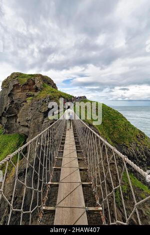 Schmale Hängebrücke für Fußgänger an der felsigen Küste, unbewohnte Insel Carrick-a-Rede, County Antrim, Nordirland, Großbritannien Stockfoto