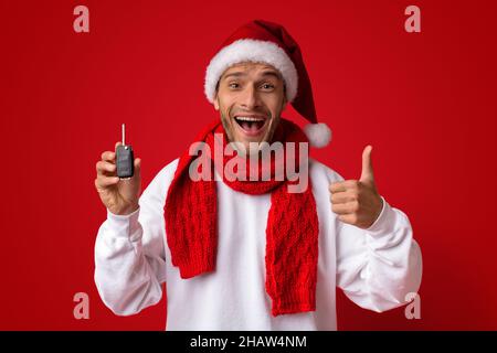 Aufgeregt Mann In Santa Hat Hält Auto-Schlüssel Und Zeigt Daumen Nach Oben Stockfoto