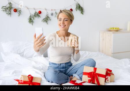 Lady mit Handy macht Videocall auf Weihnachten halten Geschenk Stockfoto