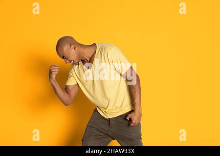 Emotionaler dunkelhäutiger Mann im T-Shirt, der isoliert auf gelbem Studiohintergrund posiert. Konzept der menschlichen Emotionen Stockfoto