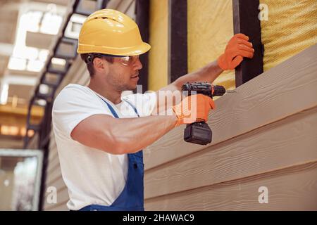 Männlicher Baumeister mit Bohrmaschine auf der Baustelle Stockfoto