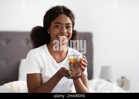 Glückliche afroamerikanische Dame, die im Bett Tee trinkt Stockfoto