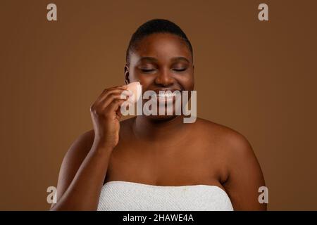 Schwarze mollige Frau mit Akne Make-up mit Schwamm Stockfoto