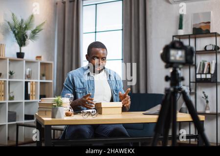 afroamerikanischer Blogger entboxend präsentieren und aufzeichnen Video vor der Kamera. Junger Mann teilt mit Abonnenten sein Feedback über modernes Gadget. Stockfoto