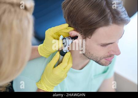 Weibliche Hände mit Otoskop in der Nähe von mans Ohr Stockfoto