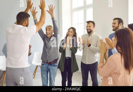 Zwei glückliche Geschäftsleute geben sich unter dem Applaus ihrer Kollegen eine doppelte fünf. Stockfoto