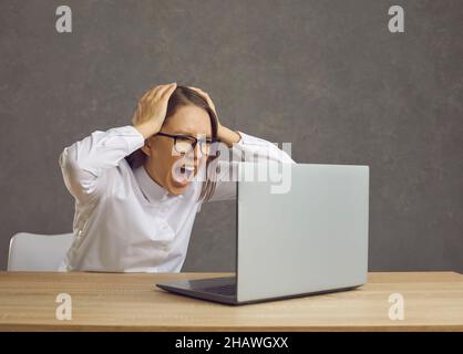 Porträt einer jungen, schockierten Frau, die Laptop-Computer ansah und schrie Stockfoto