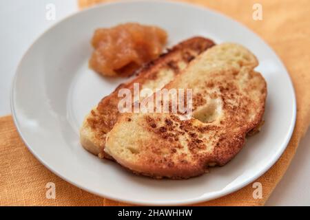 Zwei Scheiben Weißbrot, gebraten mit Ei- und Aprikosenmarmelade auf weißem Teller. Frühstückskonzept Stockfoto