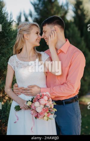 Braut und Bräutigam am Hochzeitstag zu Fuß im Freien auf Frühling Natur. Brautpaar, gerne frisch verheiratete Frau und Mann umarmen im Green Park. Liebe Hochzeit Stockfoto