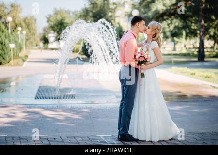 Glückliche Braut und Bräutigam auf Hochzeitswanderung in der Nähe des Brunnens. Braut und Bräutigam haben einen romantischen Moment an ihrem Hochzeitstag. Stockfoto