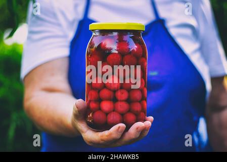 Ältere Frau mit einem Glas Kirschkompott. Hausgemachte leckere Kirschen aus der Dose im Glas. Stockfoto