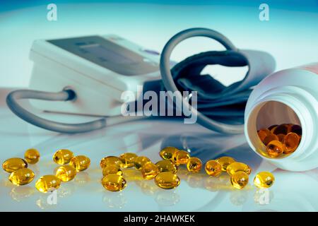 Fischöl Omega 3 Kapseln zur Vorbeugung gegen Bluthochdruck, Geräte zur Messung des Blutdrucks im Hintergrund, Tabletten aus der Flasche verschüttet Stockfoto