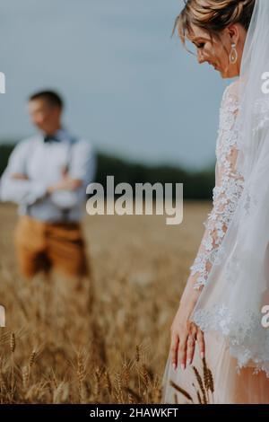 Modisches und glückliches Brautpaar am Weizenfeld an sonnigen Tagen. Braut und Bräutigam küssen im Weizenfeld. Junge schöne Hochzeit Paar umarmt in Stockfoto