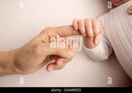 Das neugeborene Baby in einem weißen Schließen hat einen festen Griff auf den Finger der Eltern Stockfoto