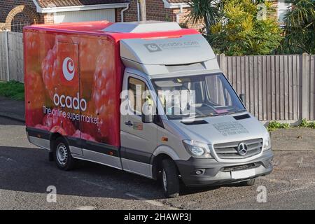 Seite & Vorderansicht Blick nach unten auf roten Mercedes Ocado Online-Lebensmittel Lebensmittel einkaufen Lieferwagen & Logo Fahrer fahren Dorf Straße Kreuzung England Großbritannien Stockfoto