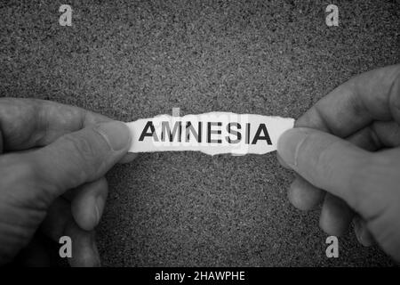 A man holding a crumpled piece of paper with the word Amnesia on it in his hands. Black and white.. Close up. Stockfoto