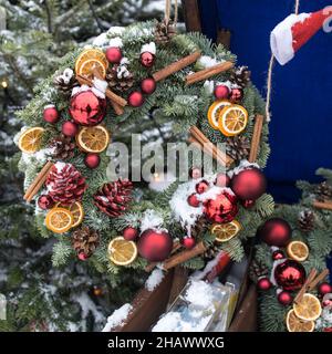 Weihnachtskranz aus Tannenzweigen mit Dekorationen, die an der Wand des Hauses hängen Stockfoto