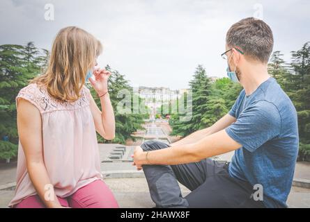 Millenial multirassischen Paar sitzt eng mit Masken auf und blickt auf Tiflis Stadt Vake Park im Hintergrund. Neuer normaler und postpandemischer Lebensstil in Stockfoto