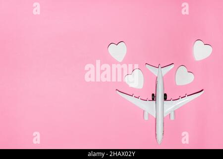 Valentinstag ist Reisekonzept. Weißes Passagierflugzeug mit Herzen auf rosa Hintergrund. Flat Lay Urlaub Planung und Reise Urlaub. Draufsicht. Stockfoto