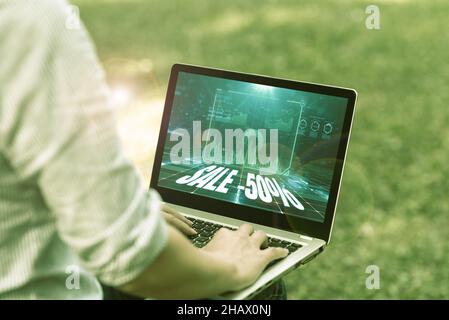 Hand schreiben Zeichen Verkauf 50 Prozent. Wort für Einen Promo-Preis für einen Artikel bei 50 Prozent Abschlag Frau auf Laptop sitzt draußen Rückansicht Arbeiten tippen Stockfoto