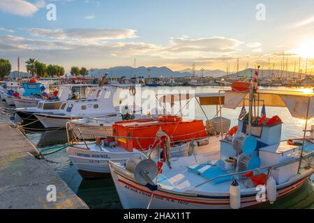 Farbenfrohe Fischerboote säumen den Hafen der griechischen Insel Aegina, Griechenland, in der Dämmerung, mit der Uferpromenade im Blick. Stockfoto