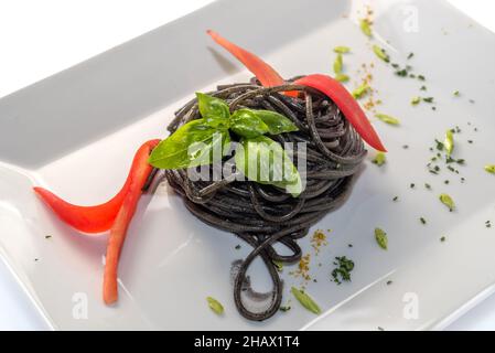 Spaghetti mit schwarzer Tintenfisch-Tinte - italienische Pasta al nero di seppia mit Basilikumblättern - aus der Nähe in einer weißen Schale isoliert auf Weiß Stockfoto